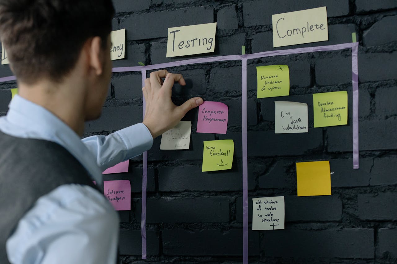 experience-img Man organizing project tasks on a wall using sticky notes in a modern office setting.
